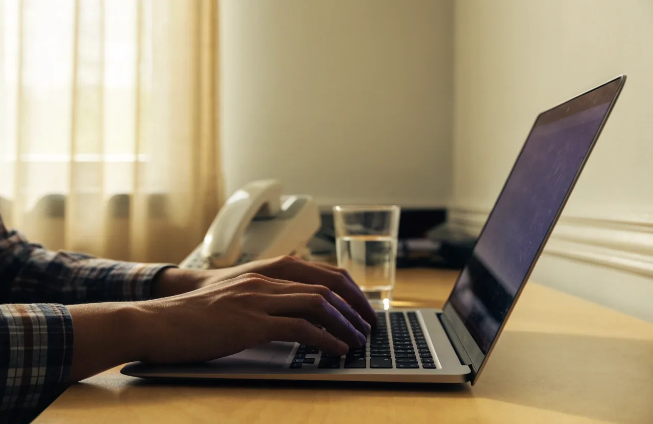 Hands typing an inquiry reply on a laptop beside a landline phone
